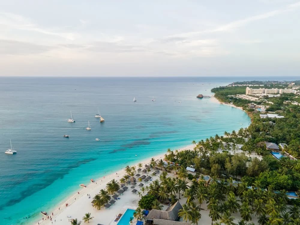 Aerial view of Kendwa Beach in Zanzibar with turquoise water, white sand, catamarans and a palm-lined shore.