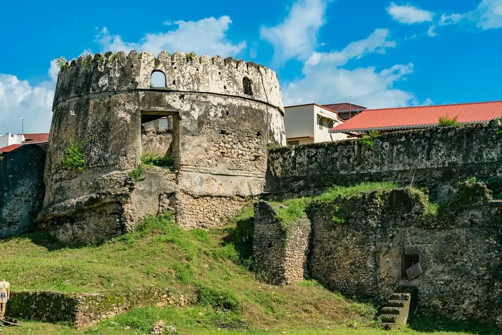 The weathered stone ramparts of the Old Fort in Stone Town, Zanzibar, under a blue sky.